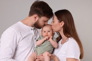 Photo of Happy family. Parents kissing their cute baby on grey background