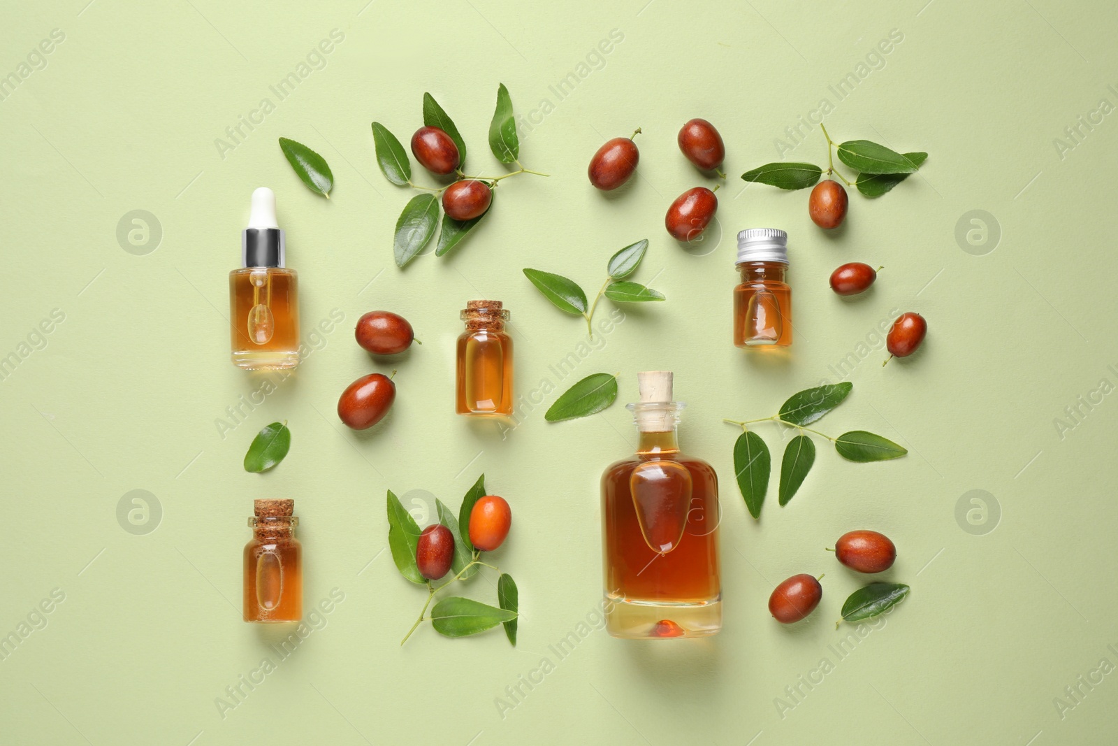 Photo of Glass bottles with jojoba oil and seeds on green background, flat lay