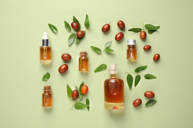 Glass bottles with jojoba oil and seeds on green background, flat lay