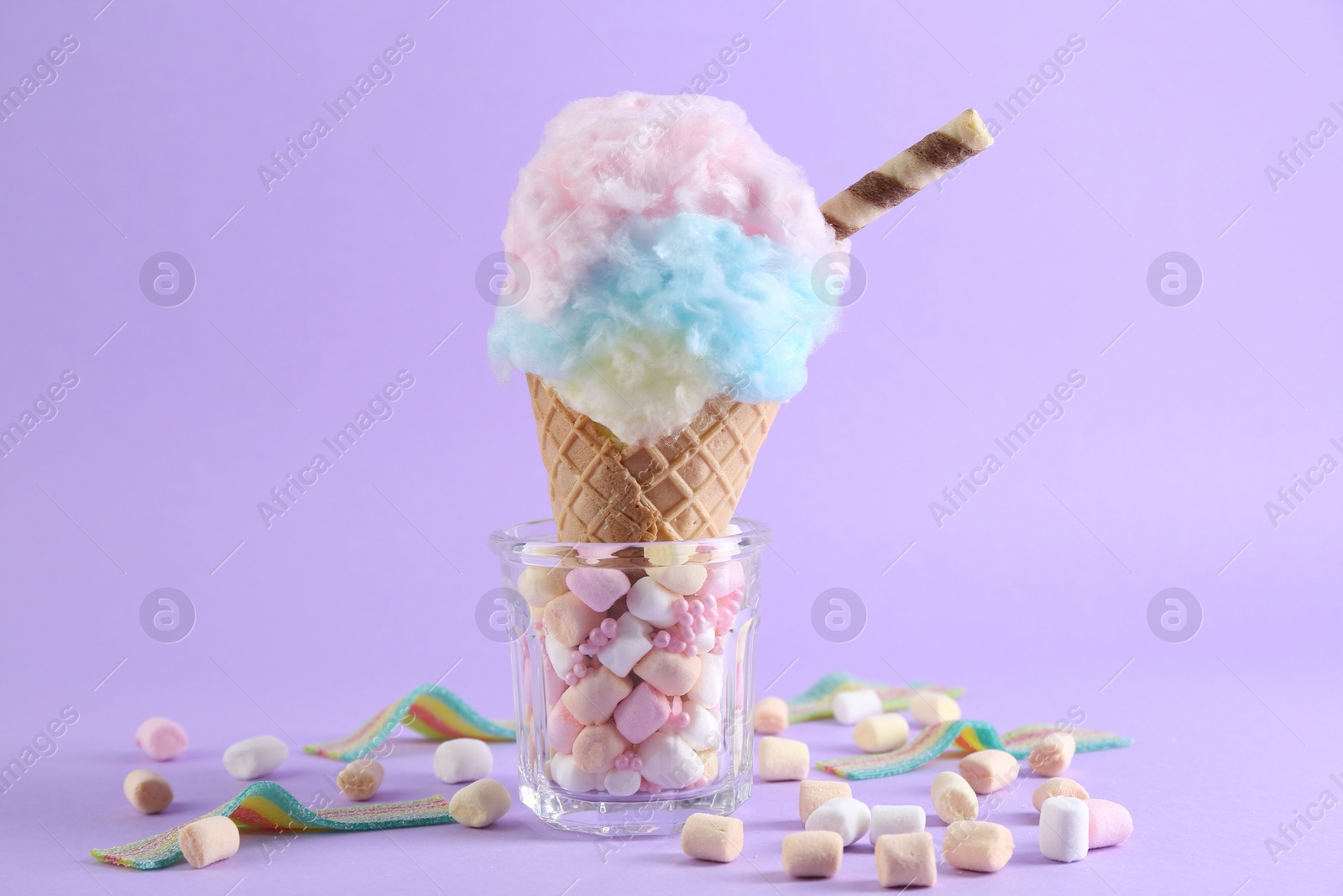 Photo of Sweet cotton candy in waffle cone and marshmallows on purple background, closeup