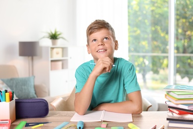 Photo of Little boy daydreaming while doing assignment at home. Stationery for school