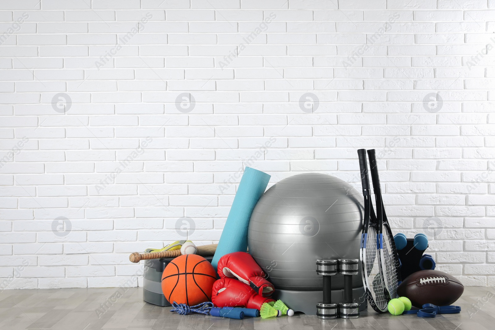 Photo of Set of different sports equipment on floor near white brick wall