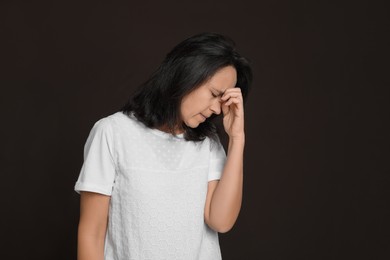 Mature woman suffering from headache on dark brown background