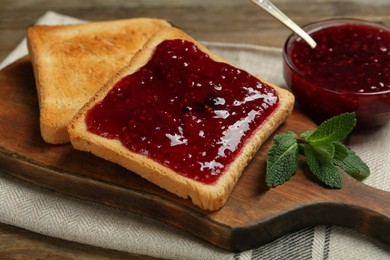 Delicious toasts with jam and mint on wooden board, closeup