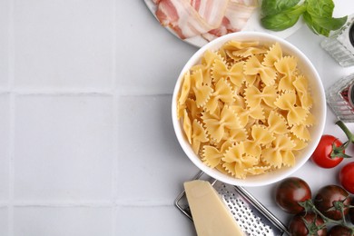 Raw pasta, bacon and fresh ingredients on white tiled table, flat lay. Space for text