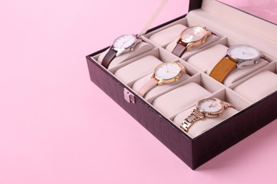 Photo of Black jewelry box with different wristwatches on pink background, closeup. Space for text