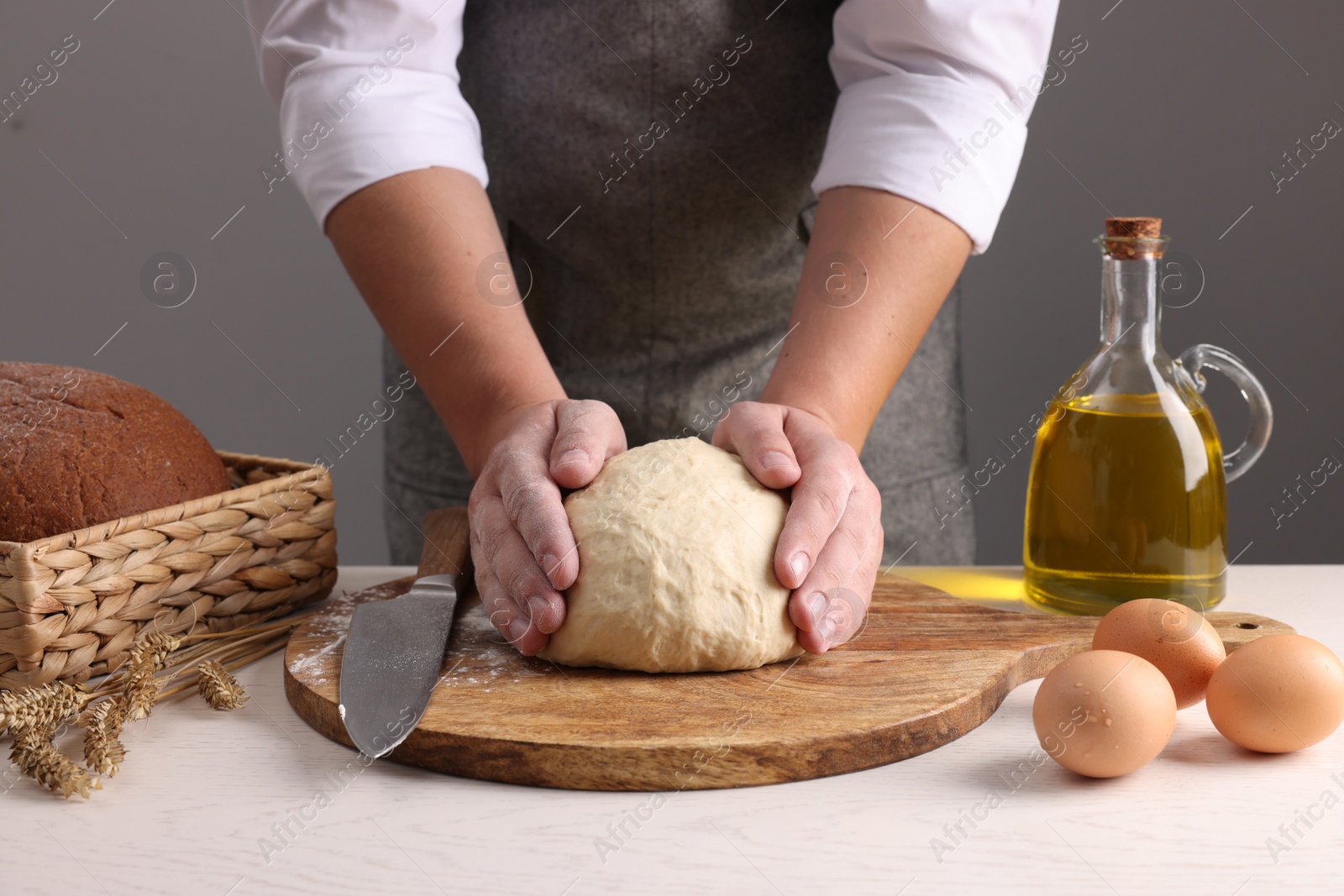 Photo of Man kneading dough at table near grey wall, closeup