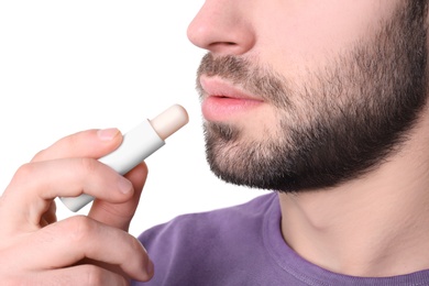 Photo of Young man applying cold sore balm on lips against white background, closeup