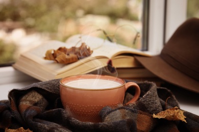 Image of Cup of hot coffee and warm scarf on window sill indoors