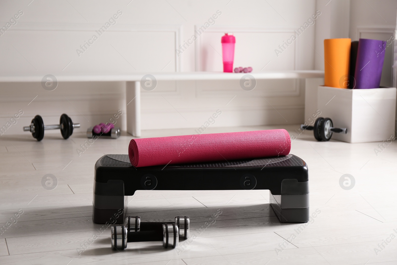 Photo of Step platform, mat and dumbbells indoors. Sports equipment