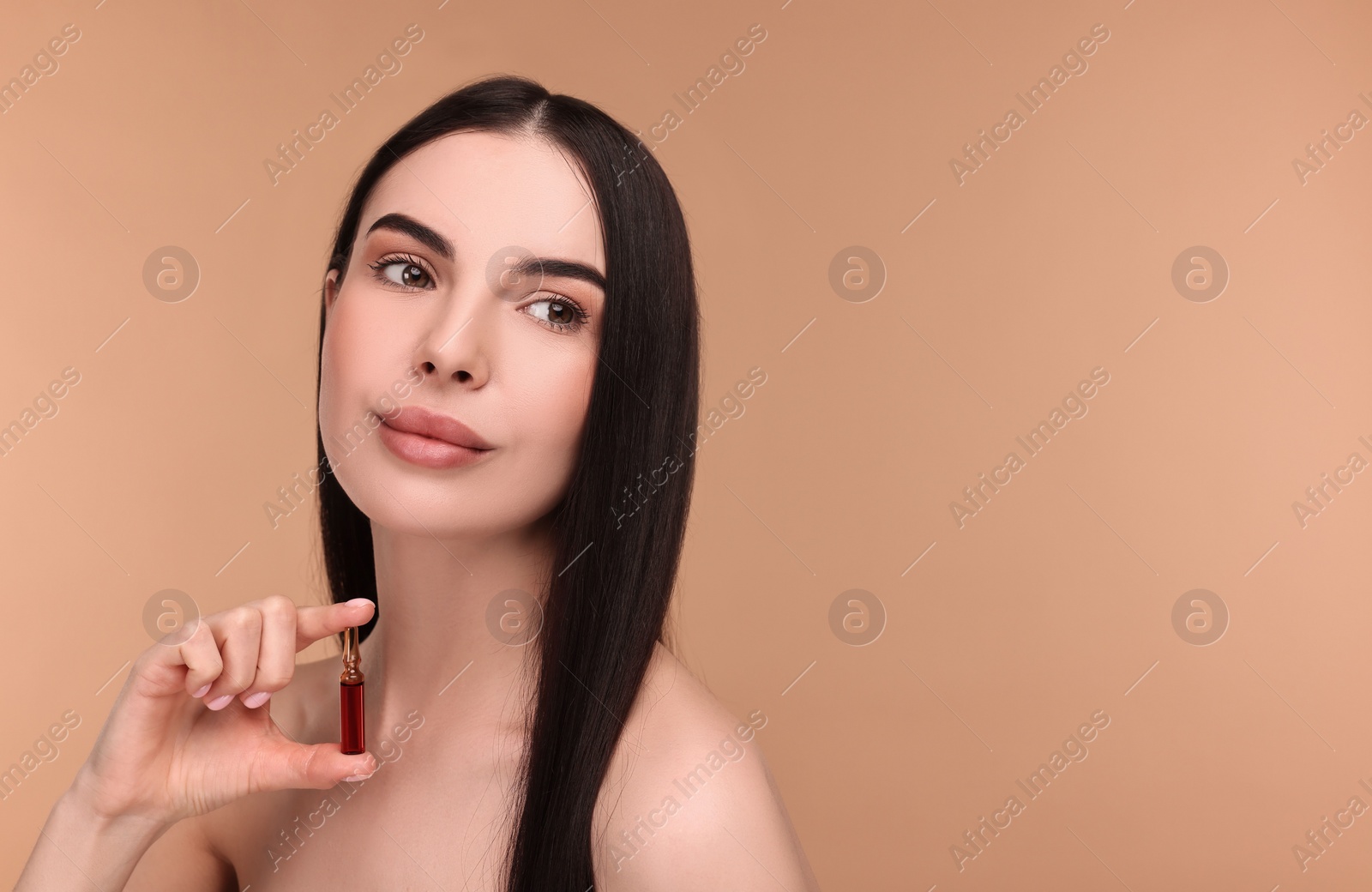 Photo of Beautiful young woman holding skincare ampoule on beige background. Space for text