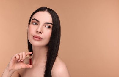 Photo of Beautiful young woman holding skincare ampoule on beige background. Space for text