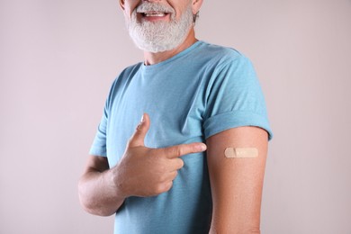 Senior man pointing at arm with bandage after vaccination on beige background, closeup