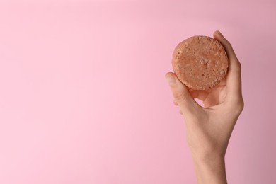 Photo of Woman holding solid shampoo bar against pink background, closeup. Space for text