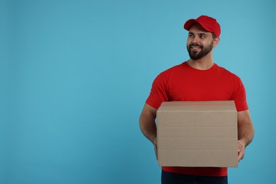 Photo of Happy young courier with parcel on light blue background, space for text