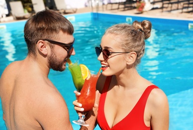 Photo of Young couple with refreshing cocktails near swimming pool at resort