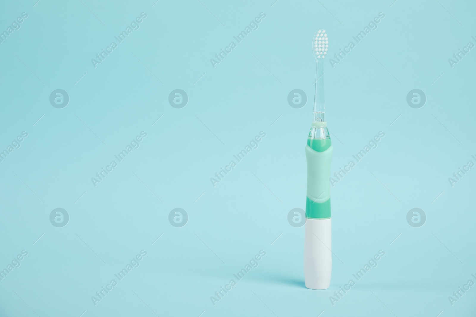 Photo of Electric toothbrush on light blue background, space for text