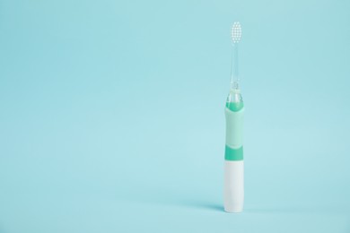 Electric toothbrush on light blue background, space for text