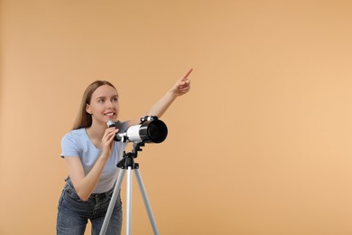 Young astronomer with telescope pointing at something on beige background, space for text