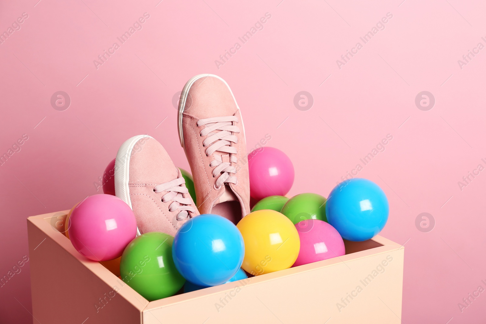 Photo of New sneakers in box with plastic balls on color background, space for text