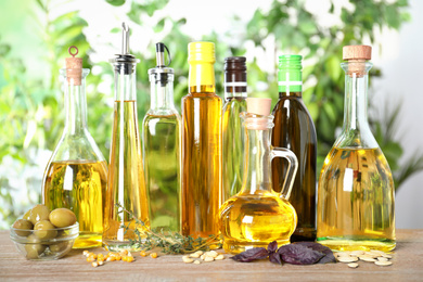 Photo of Different sorts of cooking oil in bottles on wooden table