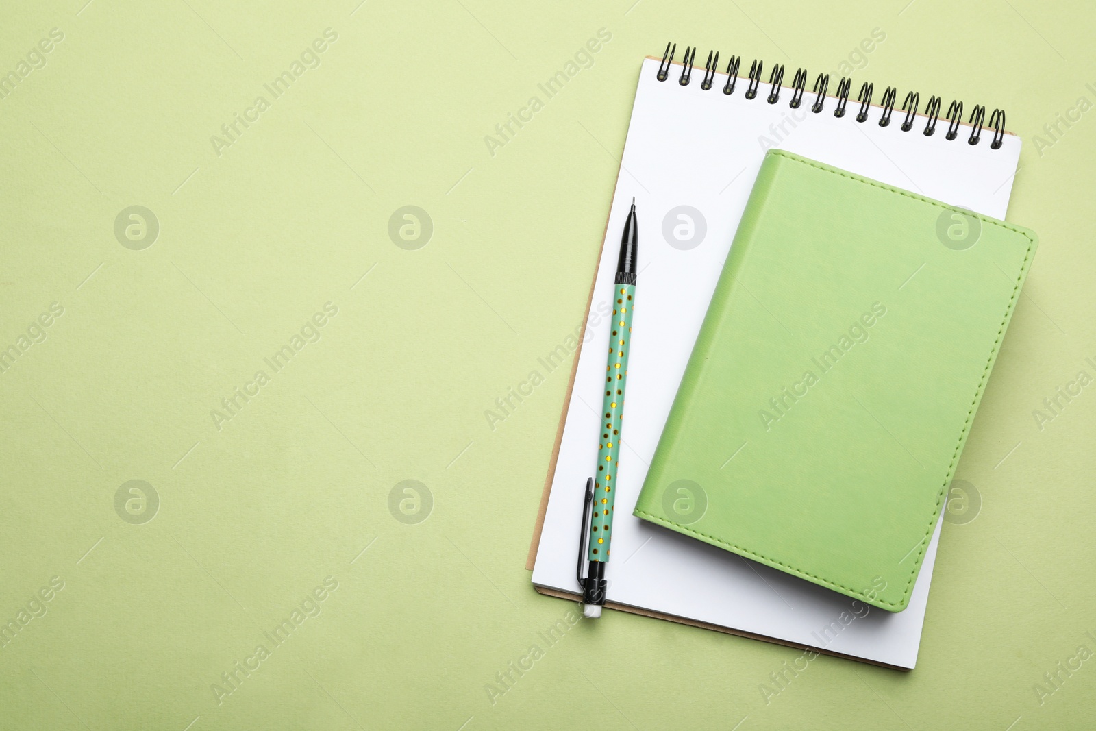 Photo of Stylish notebooks and pencil on light green background, top view. Space for text