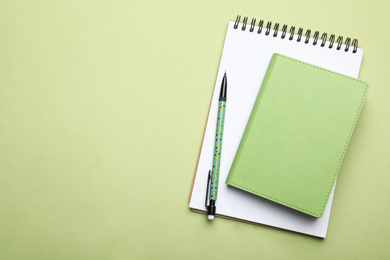 Photo of Stylish notebooks and pencil on light green background, top view. Space for text