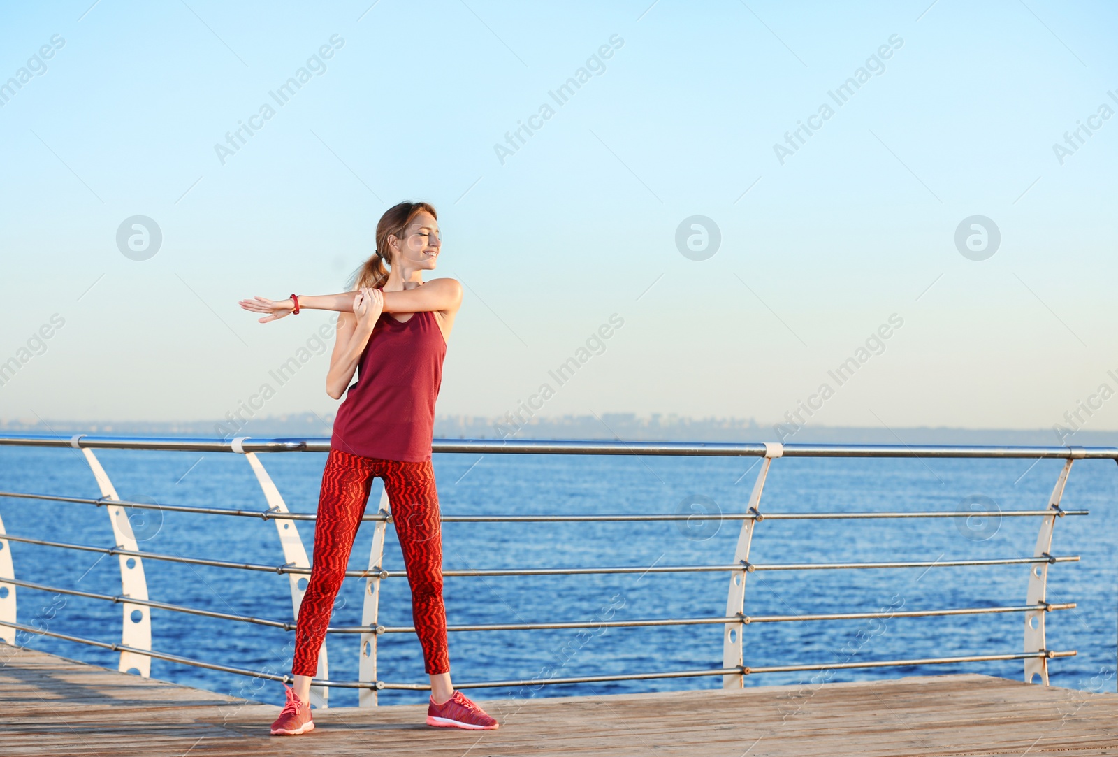 Photo of Young woman doing fitness exercises on pier in morning