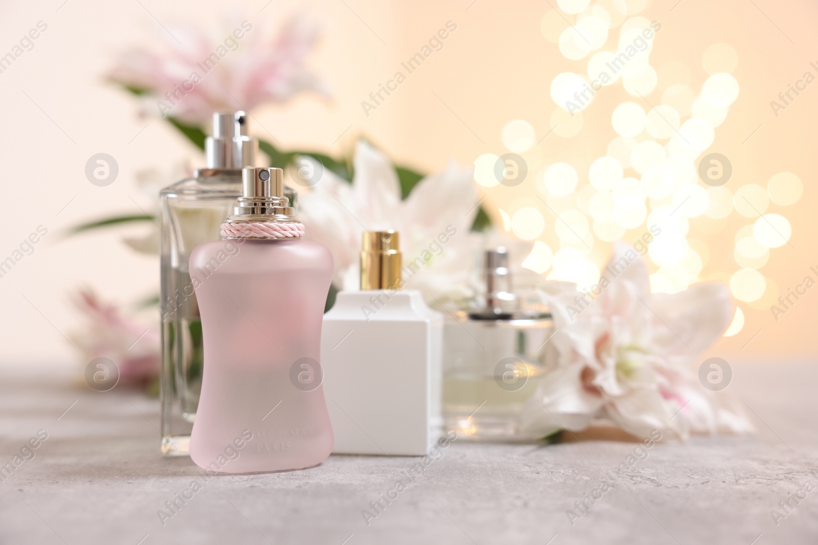 Photo of Perfume bottles and bouquet of beautiful lily flowers on table against beige background with blurred lights, closeup