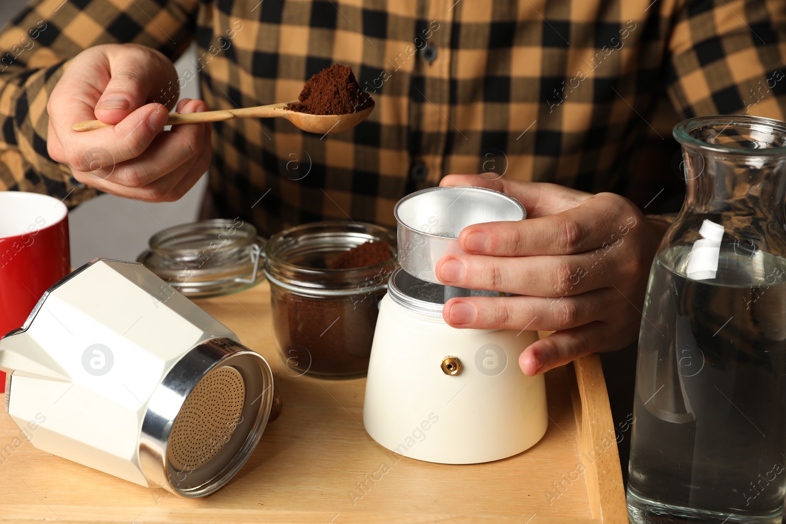 Photo of Man putting ground coffee into moka pot at table, closeup
