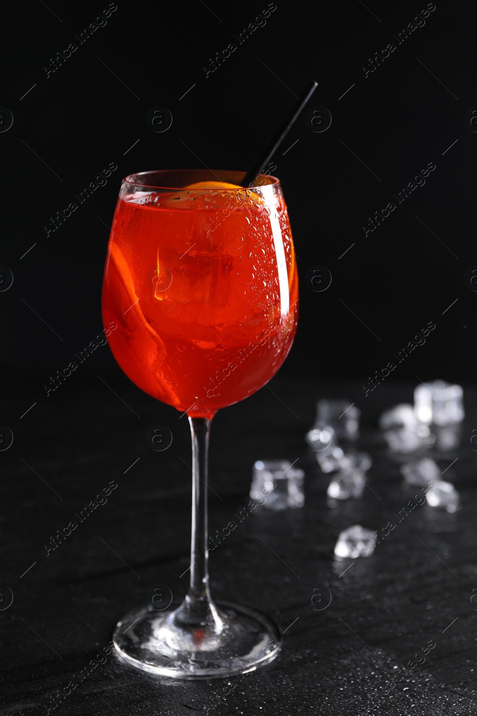 Photo of Glass of tasty Aperol spritz cocktail with orange slices and ice cubes on table against black background