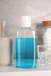 Photo of Bottle of mouthwash, toothbrush and cotton buds on white shelf in bathroom