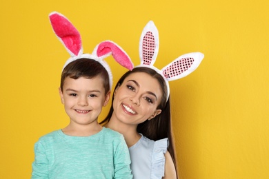 Mother and son in Easter bunny ears headbands on color background, space for text