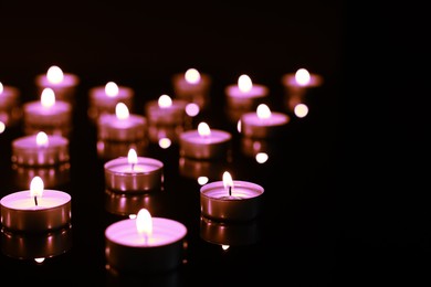 Beautiful burning violet candles on black background. Funeral attributes