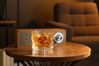 Photo of Glass of whiskey and portable speaker on wooden table in room. Relax at home