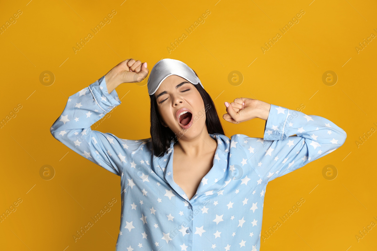 Photo of Young tired woman with sleeping mask yawning on yellow background