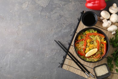 Photo of Stir-fry. Delicious cooked noodles with chicken and vegetables in bowl served on gray textured table, flat lay. Space for text