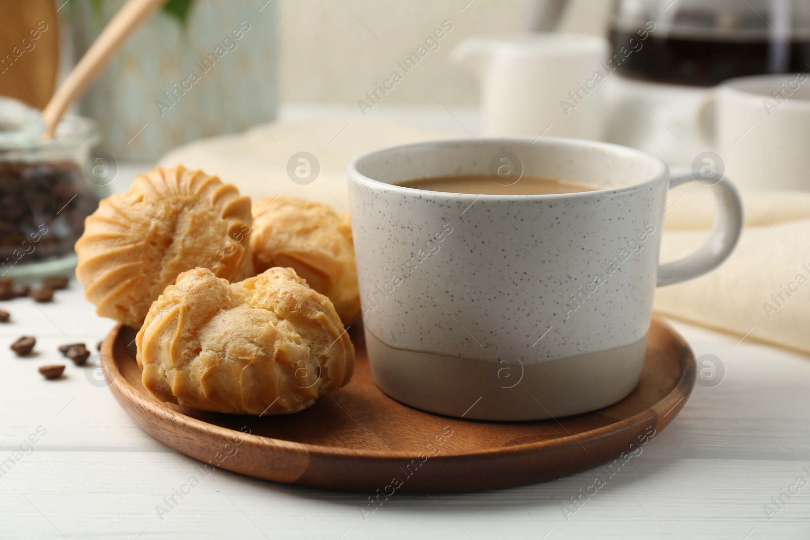 Photo of Aromatic coffee in cup and tasty profiteroles on white wooden table, closeup