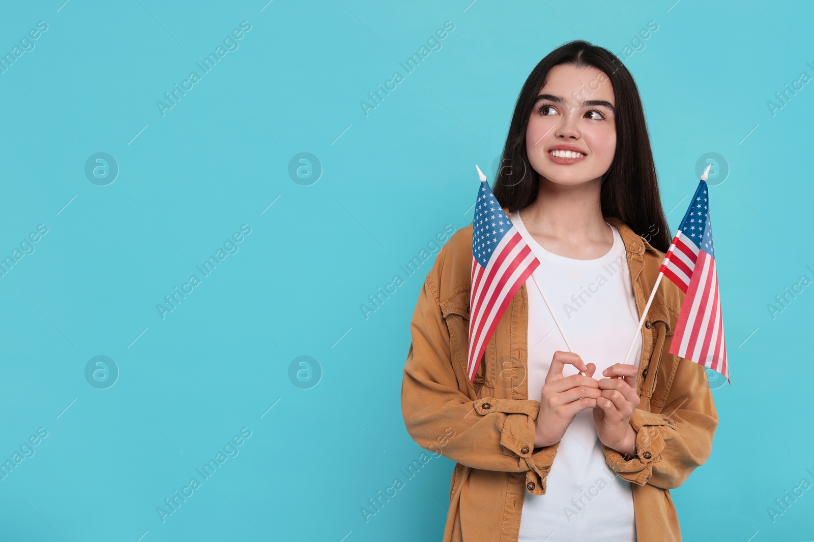 Photo of 4th of July - Independence Day of USA. Happy girl with American flags on light blue background, space for text