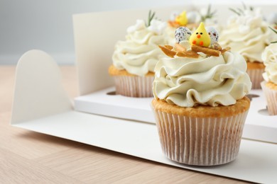 Photo of Tasty Easter cupcakes in box on wooden table, closeup