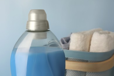 Photo of Bottle of fabric softener and terry towels in basket on light blue background, closeup