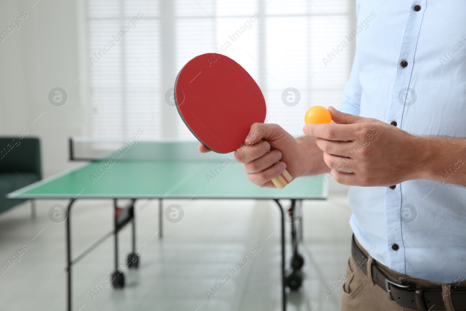 Photo of Businessman with tennis racket and ball near ping pong table in office, closeup. Space for text