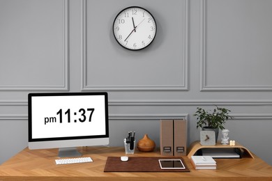 Stylish workplace with computer, houseplant and stationery on wooden desk near grey wall at home