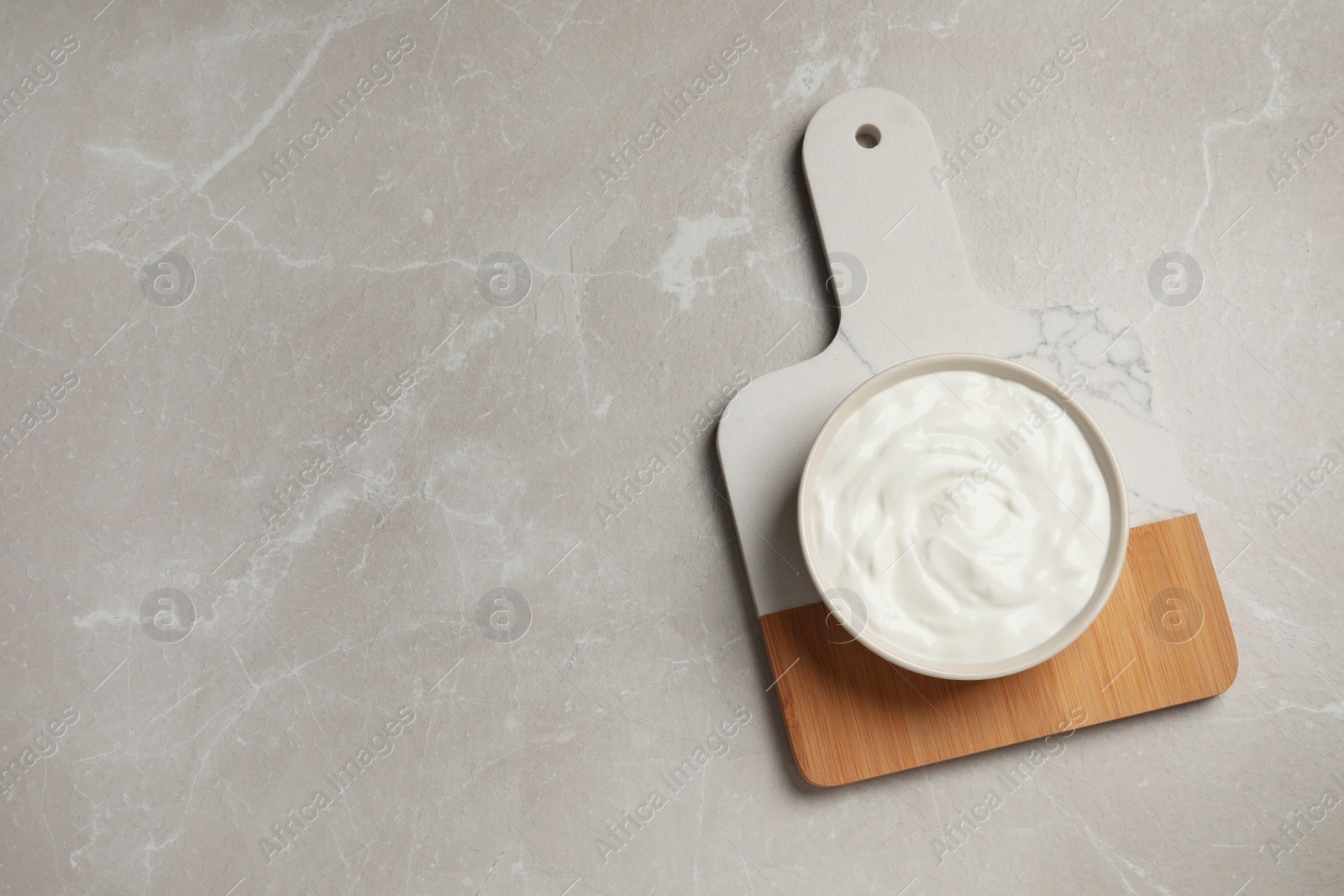 Photo of Bowl of fresh yogurt on grey table, top view. Space for text