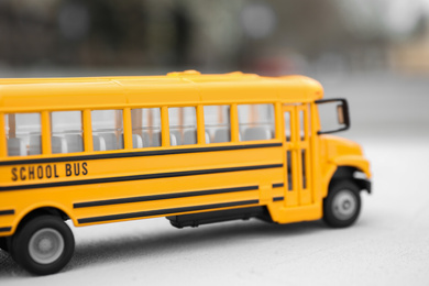 Photo of Yellow toy school bus against blurred background, closeup. Transport for students