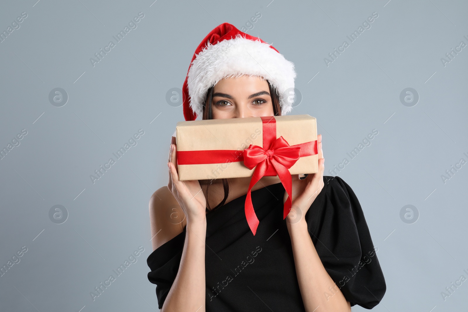 Photo of Woman in black dress and Santa hat holding Christmas gift on grey background