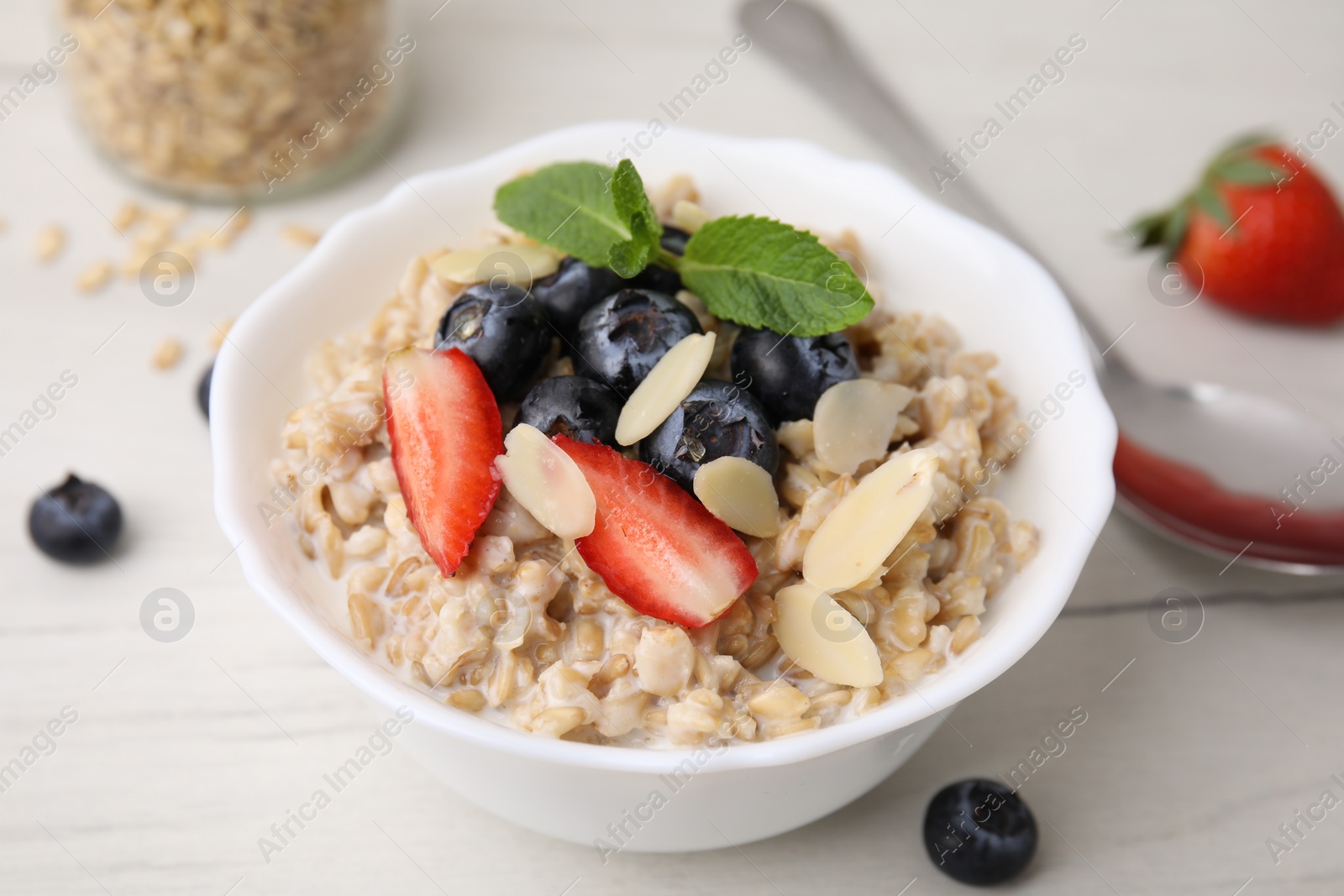 Photo of Tasty oatmeal with strawberries, blueberries and almond petals in bowl on white wooden table, closeup