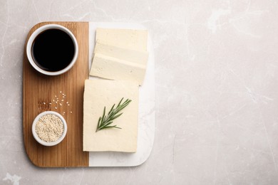 Photo of Delicious tofu with rosemary, sesame seeds and soy sauce on light table, top view. Space for text
