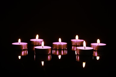 Beautiful burning violet candles on black background. Funeral attributes