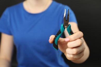Photo of Woman with bent nose pliers on dark background, closeup. Space for text